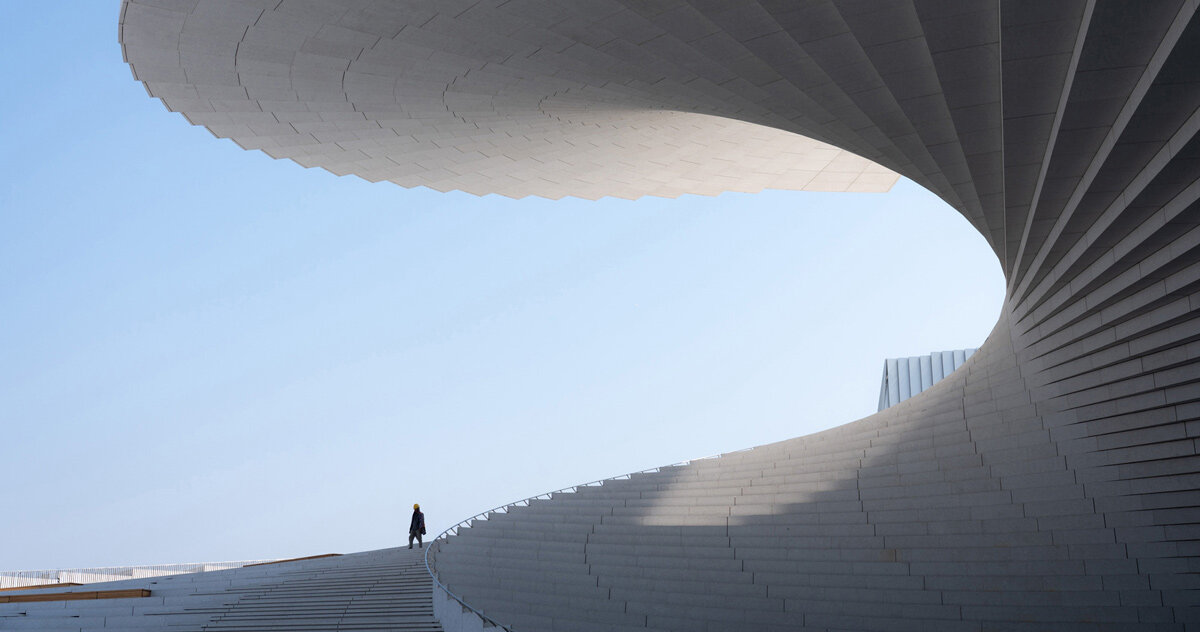 Snøhetta’s upcoming Shanghai Grand Opera House features a stunning spiral roofline over the Huangpu River, offering a dynamic space for performances with interiors inspired by traditional Chinese elements.